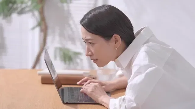 前かがみでパソコン作業をする女性
